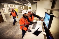 Two construction workers looking at a computer monitor.