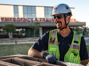 A person with construction PPE standing outside of an emergency and trauma center. 