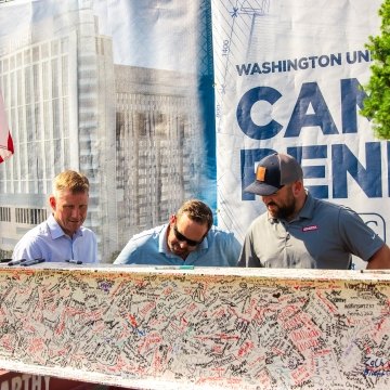 Three people signing a beam.