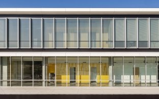 Exterior view looking through the large glass windows at a yellow wall