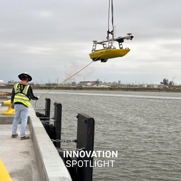 A person hoisting an unmanned survey vessel into the water