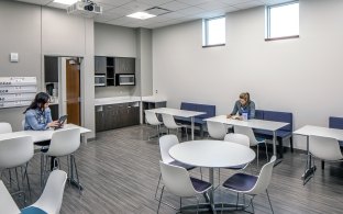 View of a sitting area with tables and chairs and a couple people sitting. 