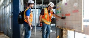 Two construction workers looking at a white board.