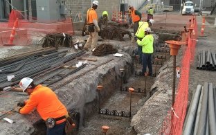 Outdoor image of workers in orange and yellow working with piping