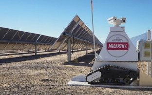 A robot in front of a few rows of solar panels