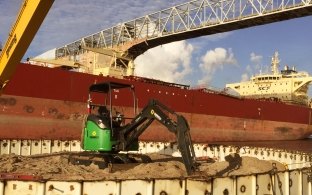 A piece of equipment at the construction site with a boat going by in the water in the background