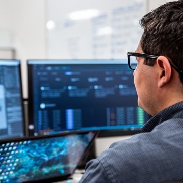 Person sitting at his desk looking at his monitors.