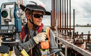 A construction worker operates survey equipment on a busy jobsite.