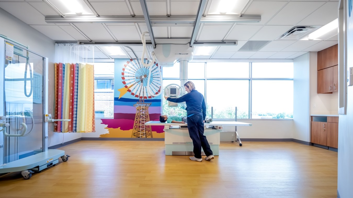 Person in patient bed with another person standing next to the bed