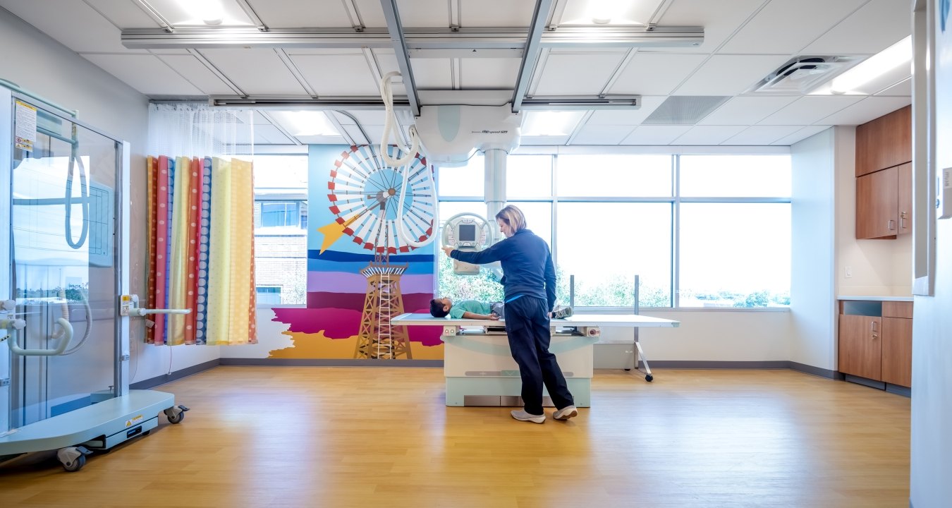 Person in patient bed with another person standing next to the bed