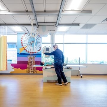 Person in patient bed with another person standing next to the bed