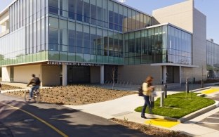 UC Davis, Student Health & Wellness Center Exterior With People Walking and Riding a Bike