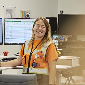 Person standing by her desk smiling at the camera.