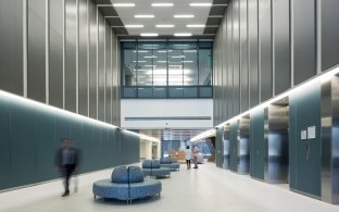 People walking through an elevator lobby with tall ceilings