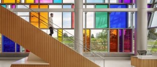 A person walking down an interior staircase, with colorful glass windows in the background.